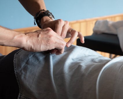 A close-up of a person's hands performing a chiropractic adjustment, gently manipulating the clothing of a patient lying face down on a treatment table.